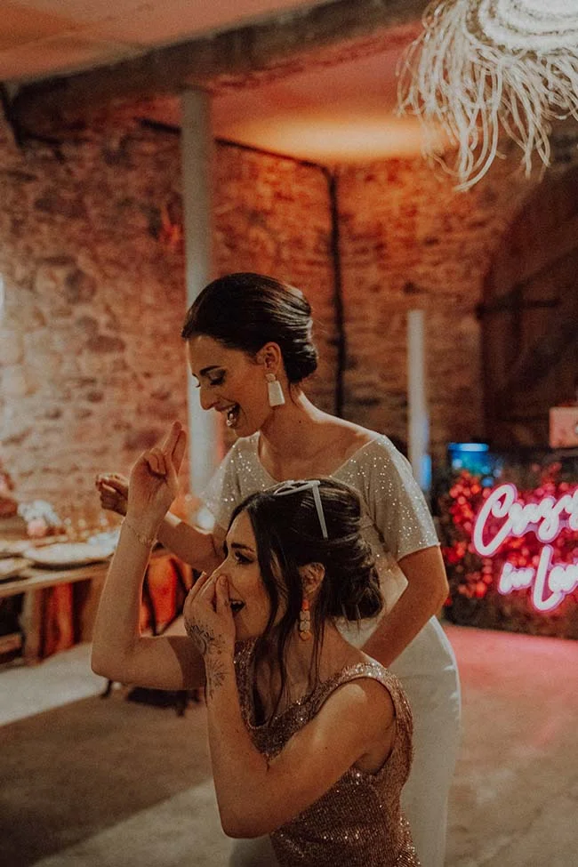 Deux femmes rient avec enthousiasme lors d'une soirée mariage disco aux tons chauds et lumineux.