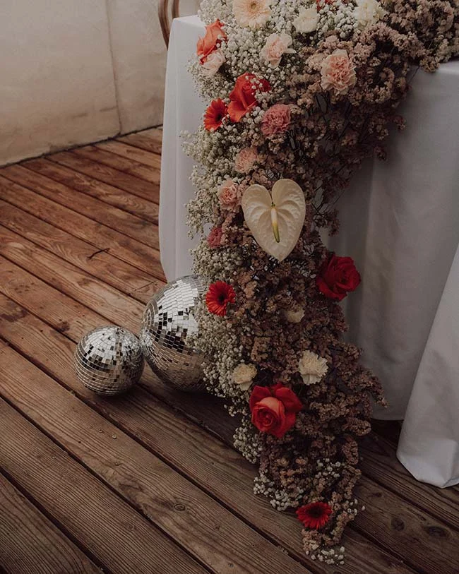 Cascade florale aux tons rouges et blancs et boules à facettes sur un parquet en bois pour un mariage disco rétro.