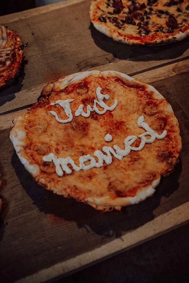 Une pizza sur une table en bois avec l'inscription Just Married écrite en sauce blanche.