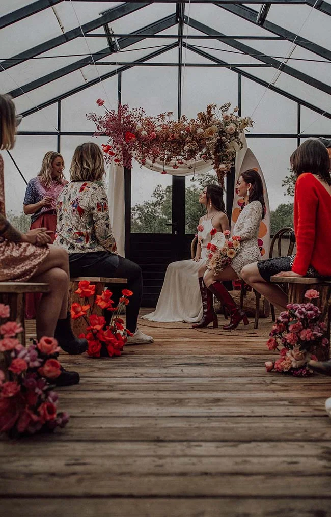 Cérémonie de mariage rétro dans une serre avec décoration florale rouge et invités aux styles colorés et vintage.