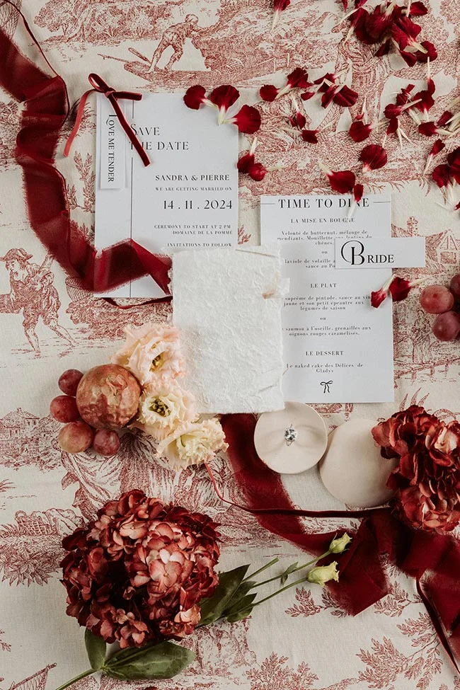 Papeterie de mariage élégante avec fleurs rouges et blanches sur fond illustré, ambiance romantique et hivernale.