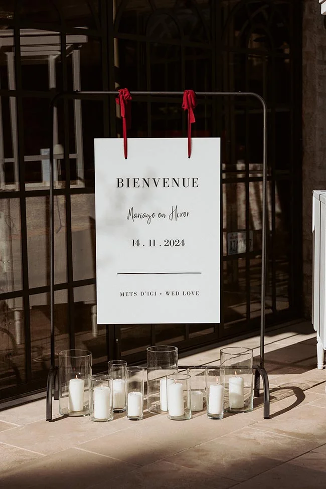 Panneau de bienvenue blanc et bougies blanches sur un support noir pour un mariage hivernal élégant.
