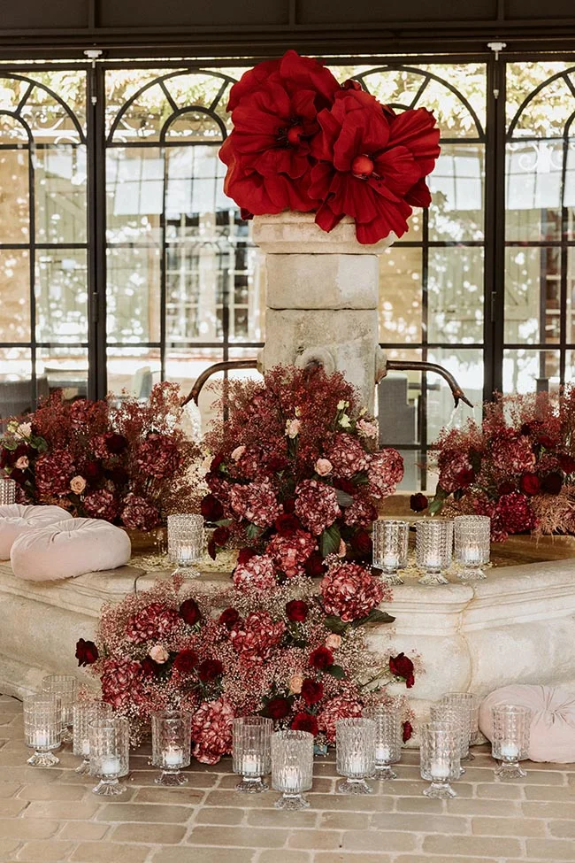 Décoration florale rouge intense et bougies entourant une fontaine en pierre pour un mariage hivernal en Provence.