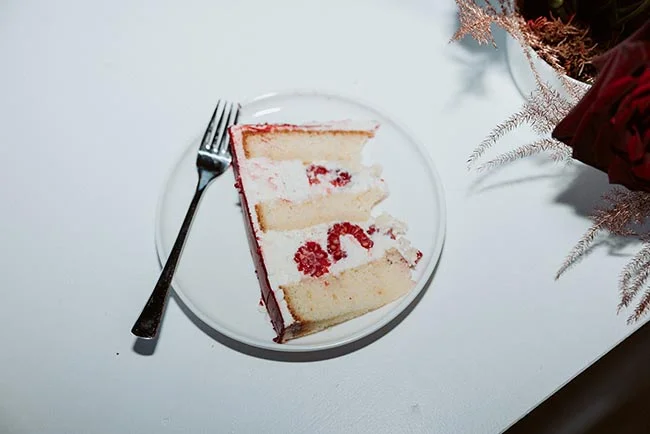 Une part de gâteau blanc et rouge sur une assiette blanche, accompagnée d'une fourchette et de roses rouges.
