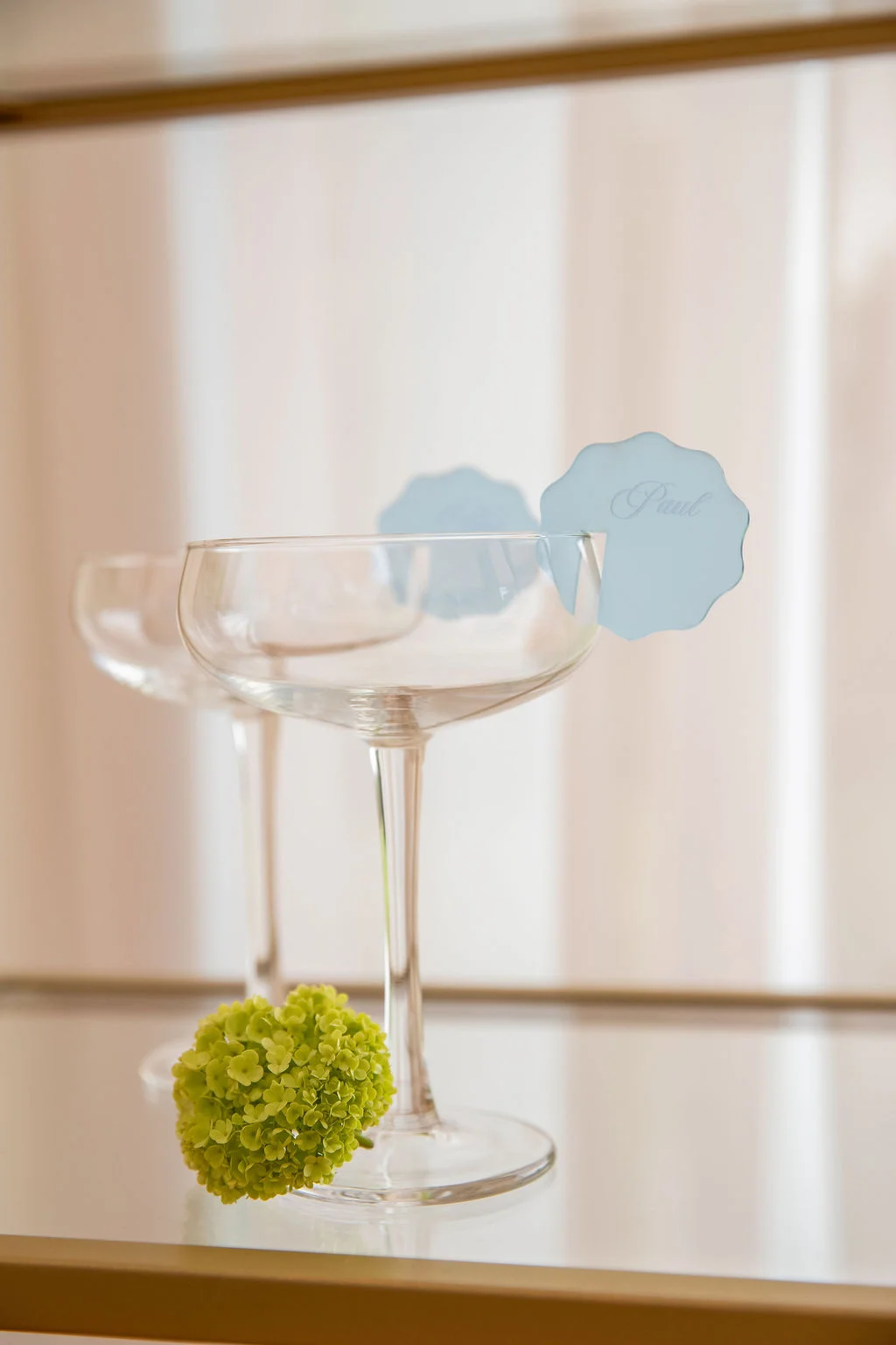 Deux coupes de champagne et un marque-place bleu pastel accompagnés d'une fleur verte sur un plateau miroir.