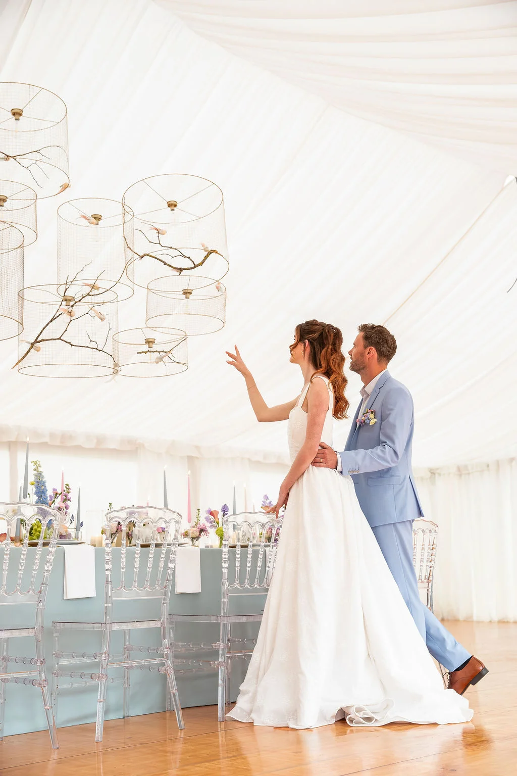 Jeunes mariés admirant la décoration aérienne et romantique d'une réception sous un chapiteau blanc.