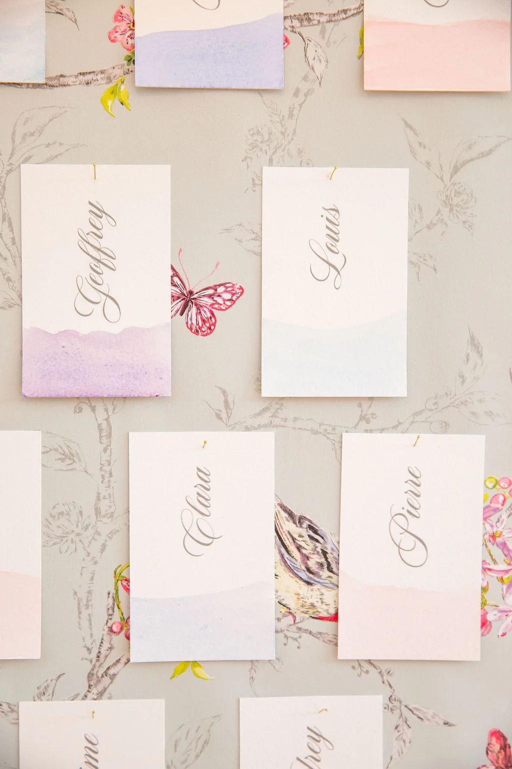 Marque-places calligraphiés aux tons pastel et aquarelles, disposés sur un fond floral romantique et épuré.