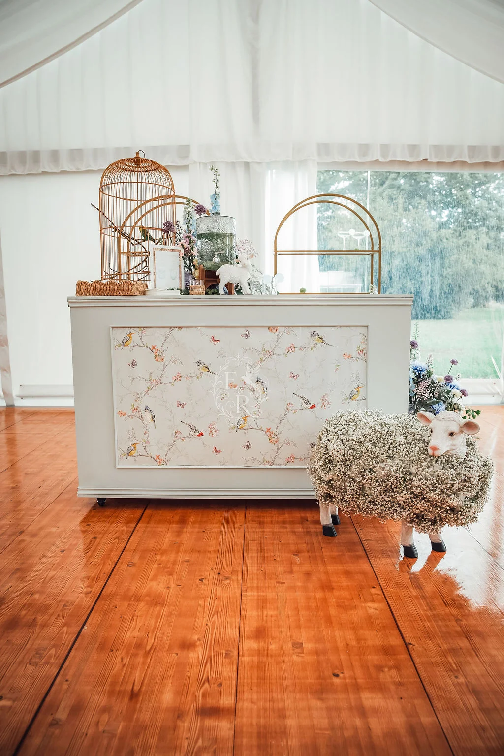 Bar romantique blanc décoré d'oiseaux, d'une cage dorée et d'un mouton en fleurs sur un parquet chaleureux.
