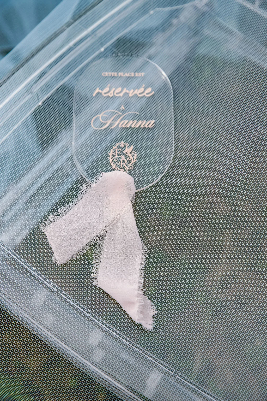 Marque-place en acrylique transparent personnalisé au nom de Hanna avec un ruban blanc sur un fond de tulle vaporeux.