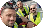 Drei Männer mit Sicherheitswesten nehmen ein Selfie in einer urbanen Umgebung.
