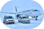 Zwei weiße Autos stehen bei Schnee vor einem Flugzeug auf einer vereisten Startbahn.