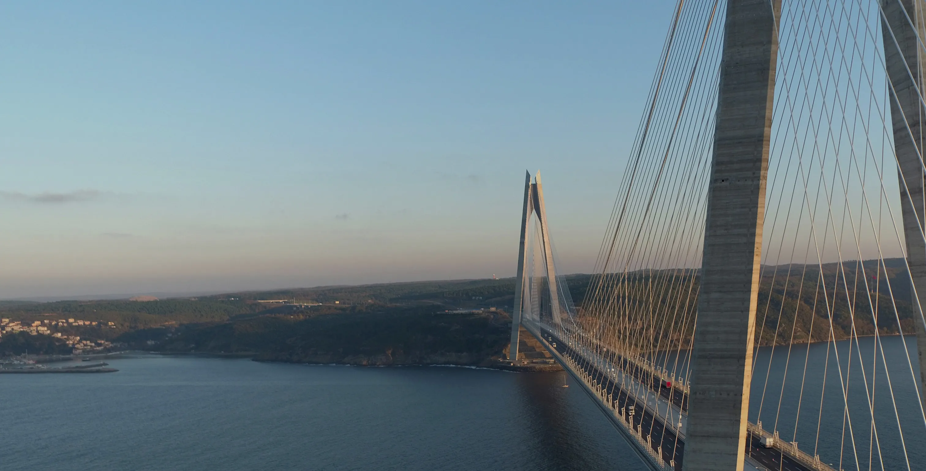 Seilbrücke über ein großes Gewässer mit bewaldeten Hügeln im Hintergrund bei klarem Himmel.