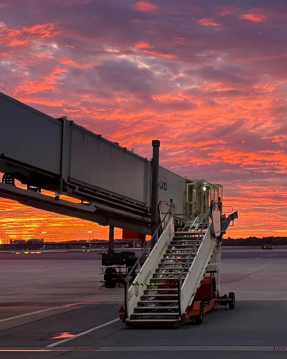 Leere Flugzeug-Gangway bei Sonnenuntergang mit orange-rotem Himmel auf Flughafenrollfeld.