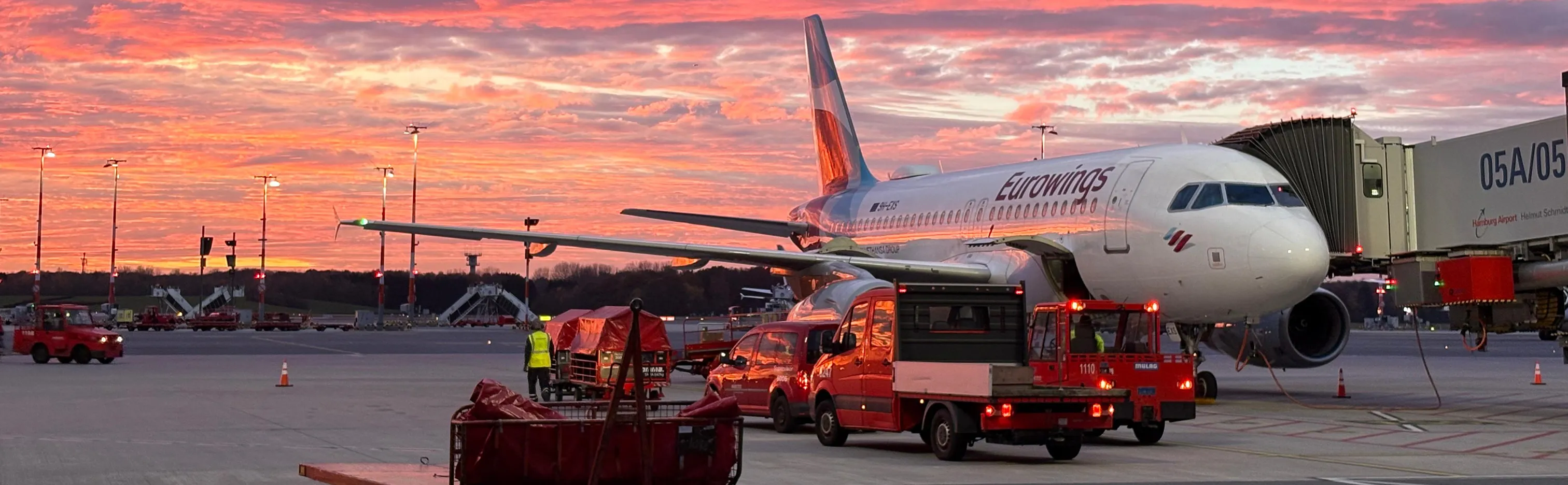 Eurowings-Flugzeug an einem Gate am Flughafen Hamburg bei Sonnenuntergang, mit Bodenpersonal und Fahrzeugen.