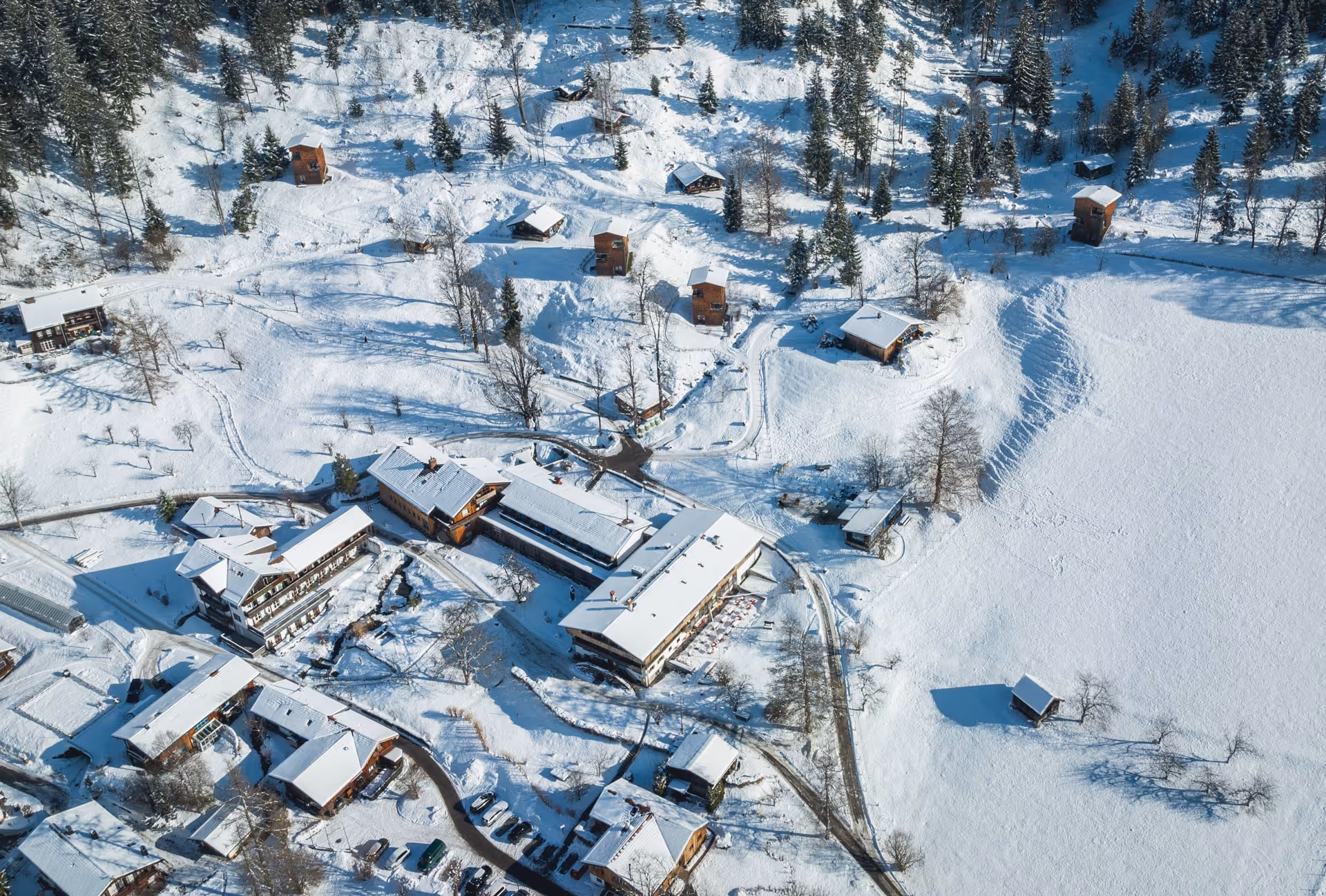 Aerial view of snow-covered buildings, trees, and pathways in a winter landscape.