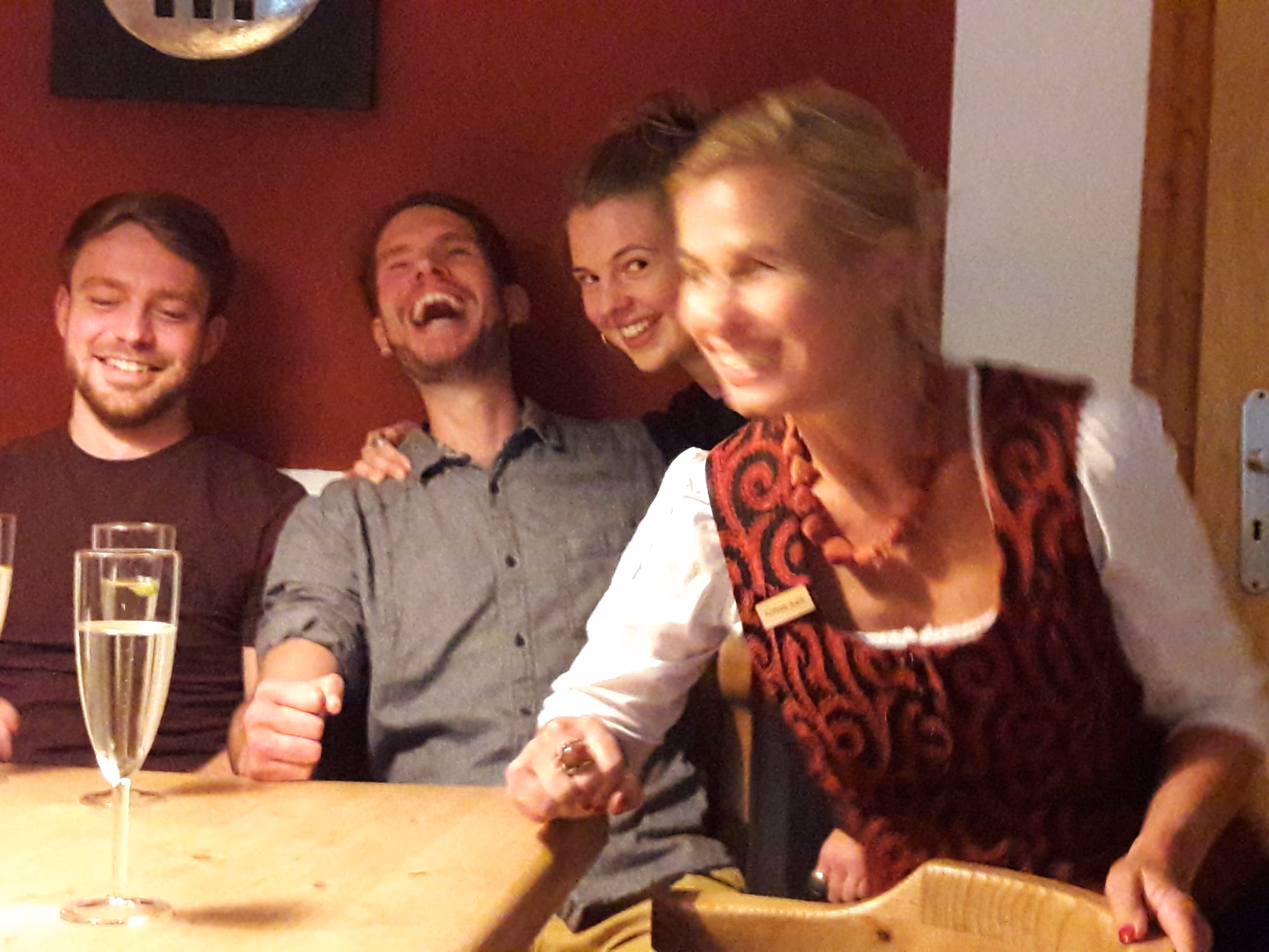 Vier lachende Menschen sitzen an einem Tisch mit Gläsern, Freude bei einer Feier spürbar.