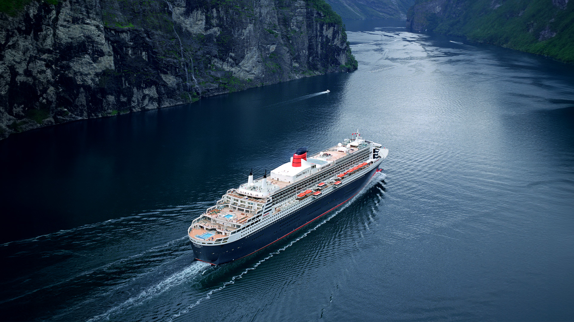 Luxury cruise ship sailing through a fjord surrounded by steep mountain cliffs.