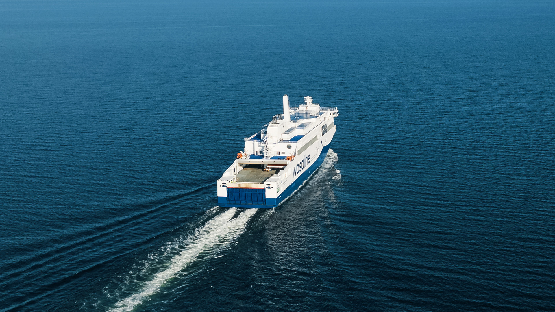 Aerial view of a ferry vessel traveling across open sea leaving a wake behind.