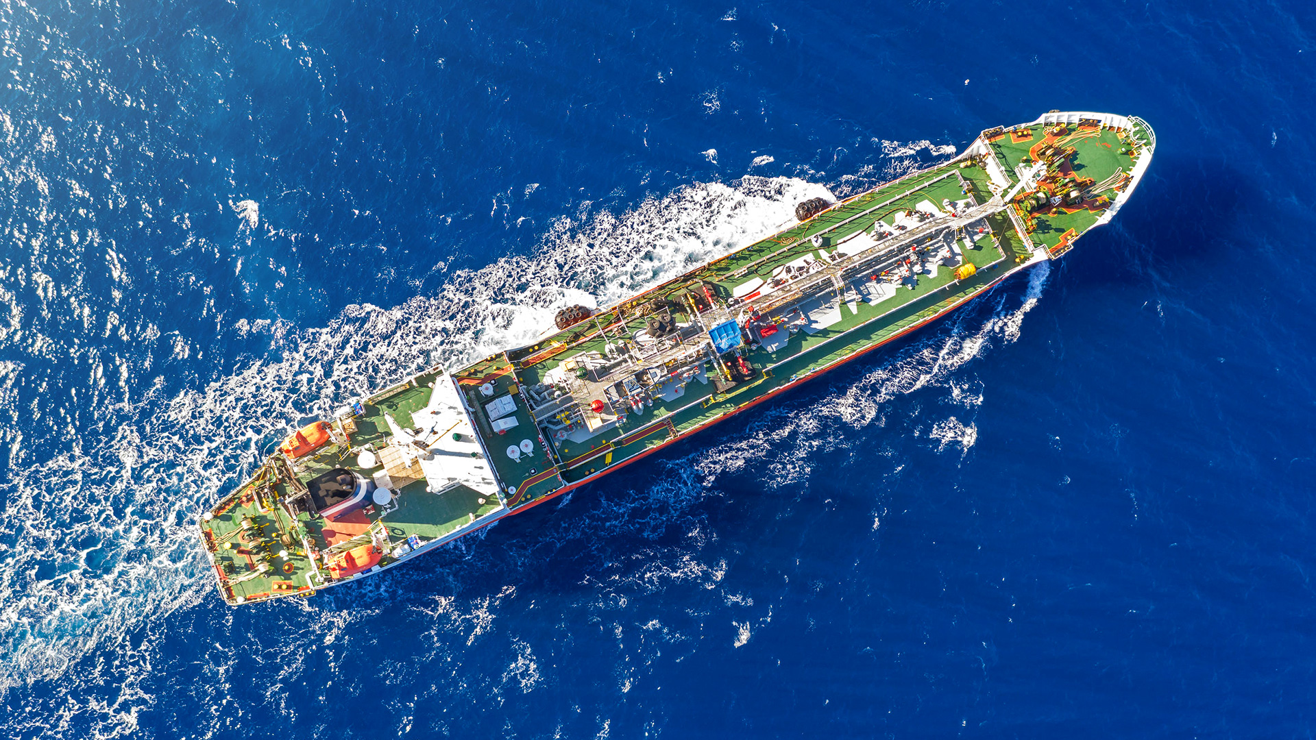 Aerial top view of an offshore support vessel operating in deep blue ocean waters.
