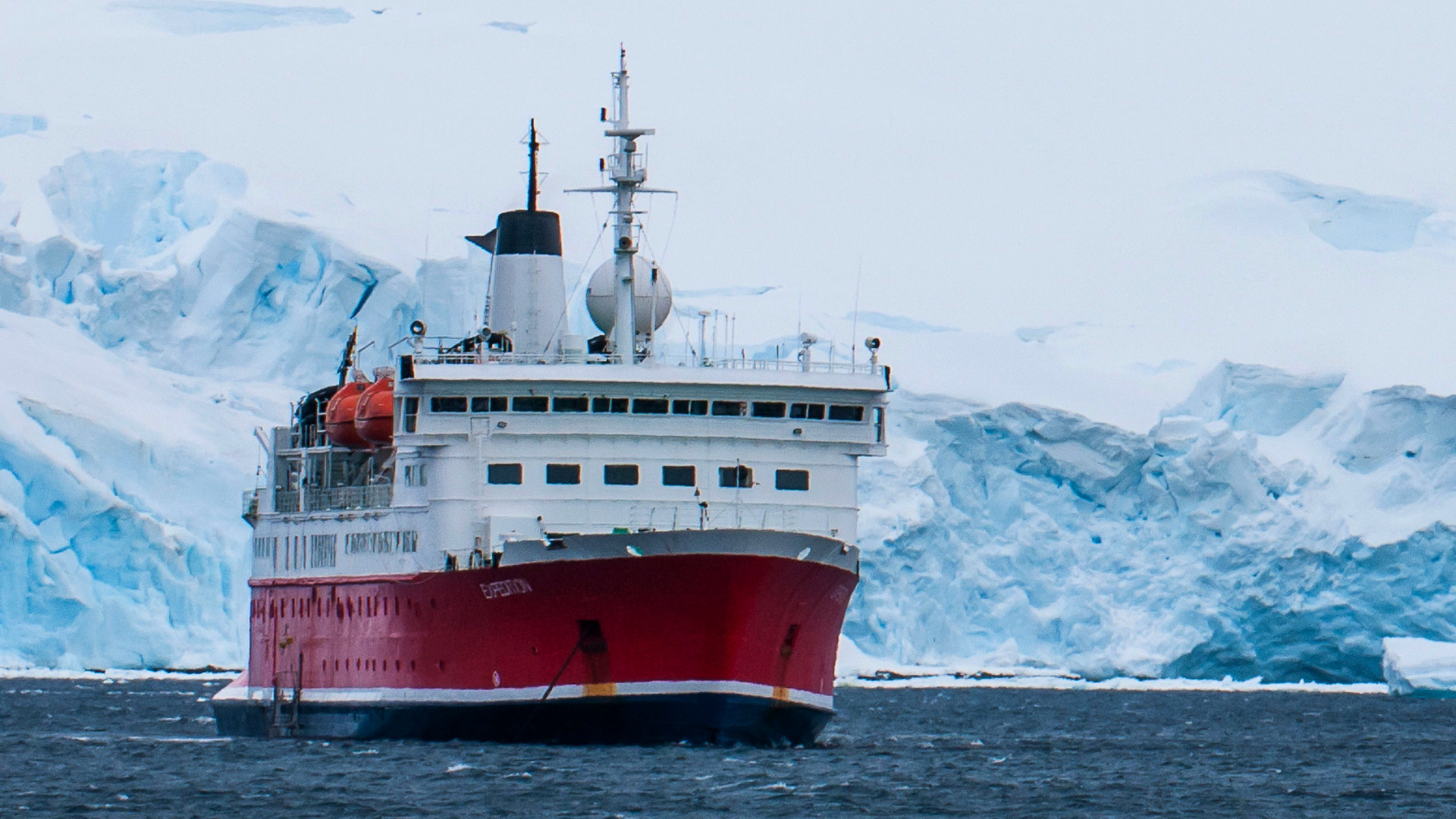 Specialised expedition vessel navigating icy waters near glacier formations in polar conditions.