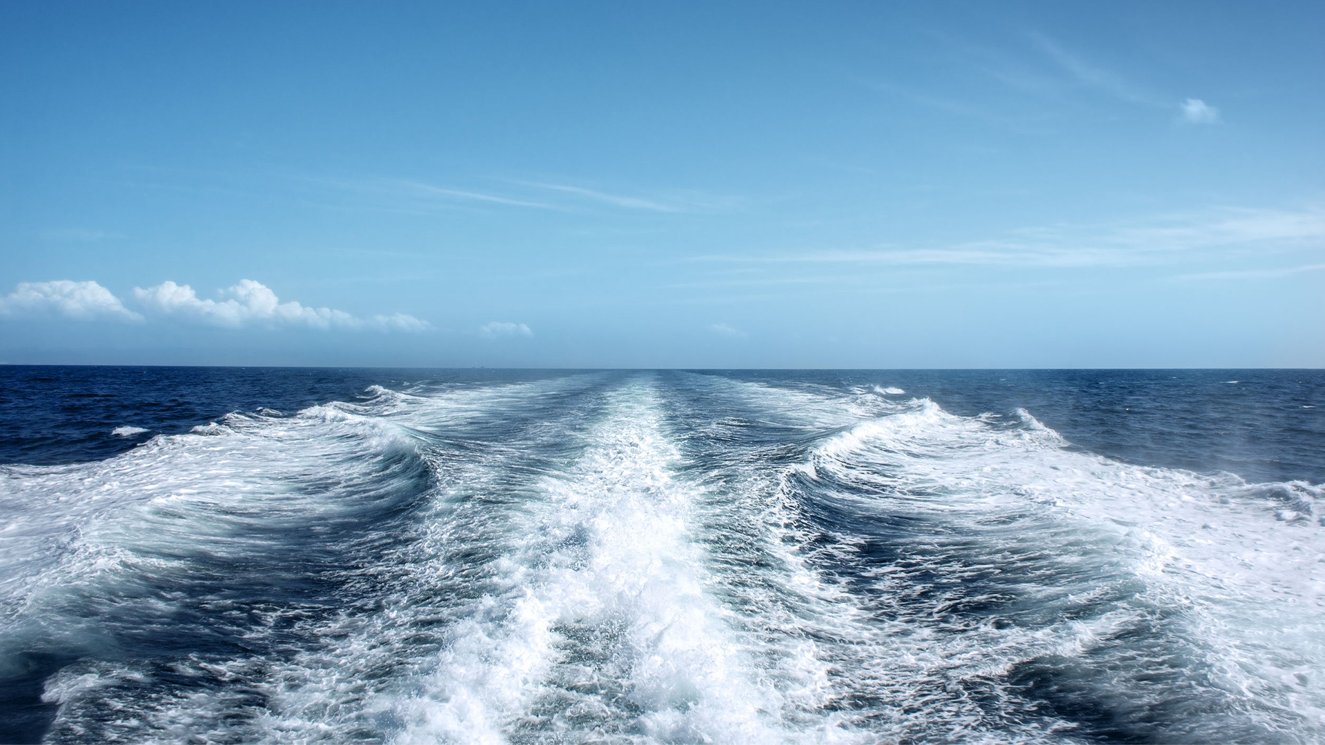 Ocean wake trail created by a moving ship across open sea under a clear blue sky.