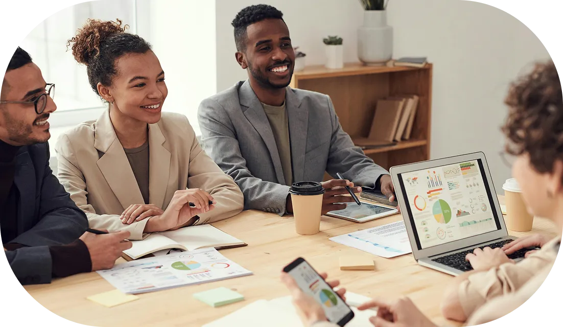 Smiling business team reviewing charts and data on laptop, tablet, and smartphone in a meeting.