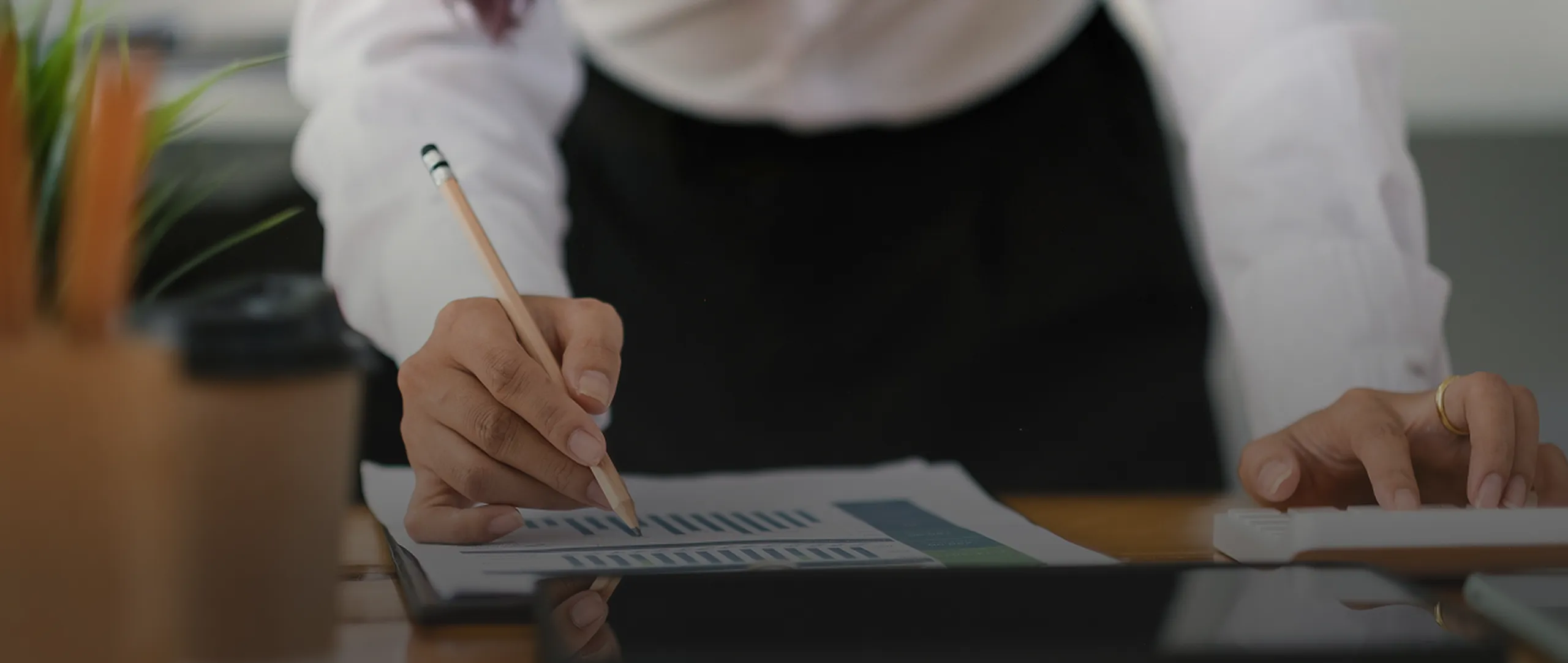 Person in white shirt pointing with pencil at bar charts on paper while typing on keyboard.
