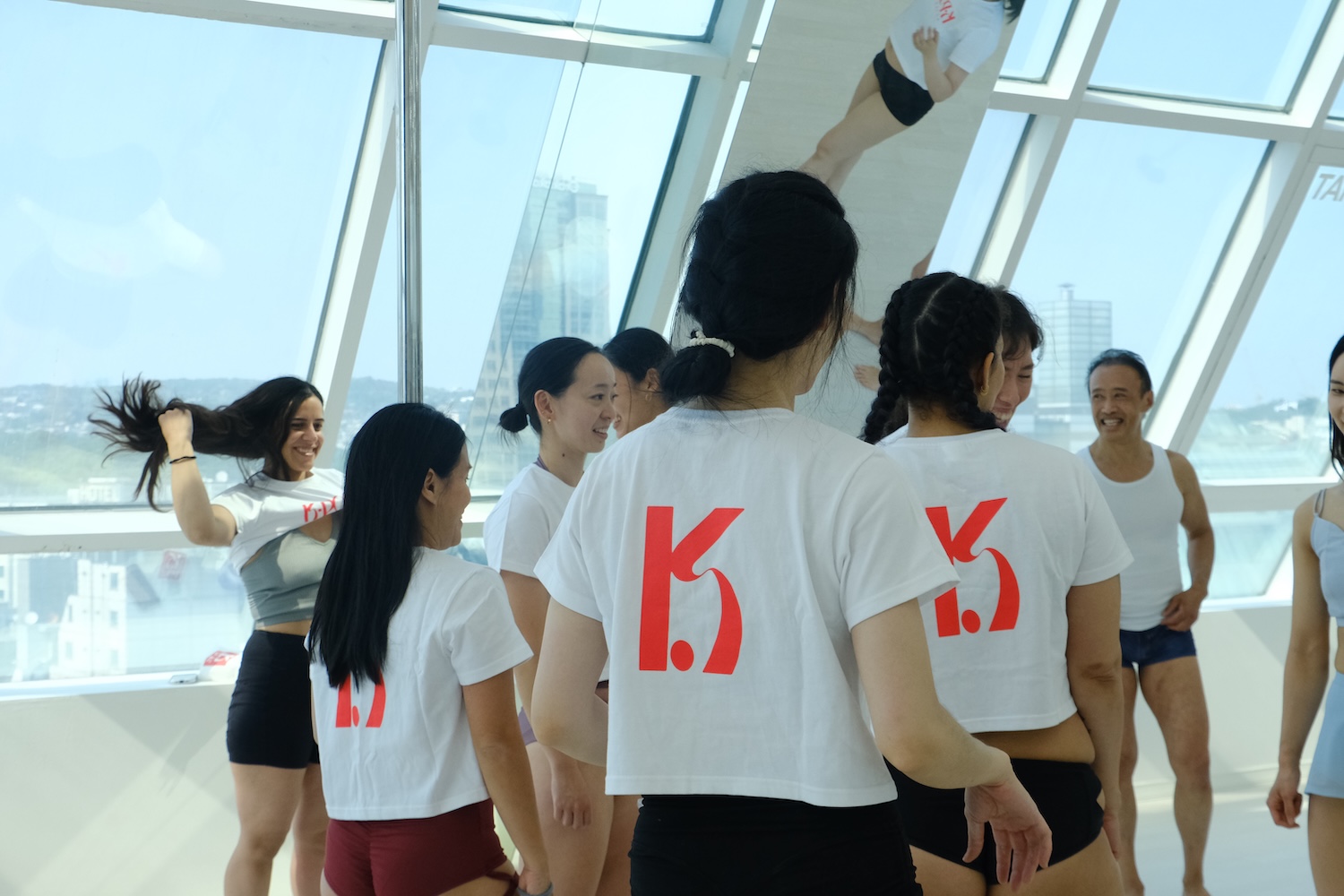 Retreat participants wearing K-Pole merch and chatting in a bright studio with large windows in Seoul.