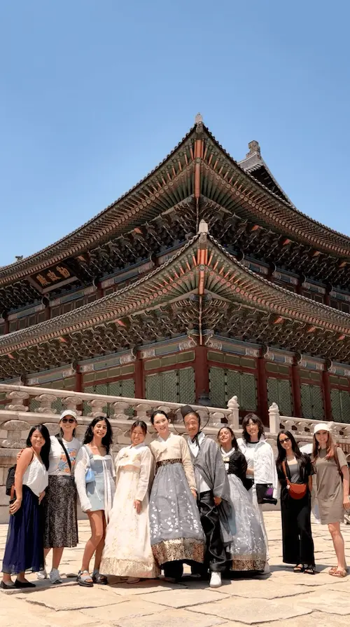 K-Pole Retreat participants, some in traditional Korean hanbok, posing in front of a historic palace with clear sky in Seoul.