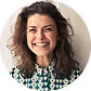 Smiling woman with curly hair wearing a patterned shirt against a light background.