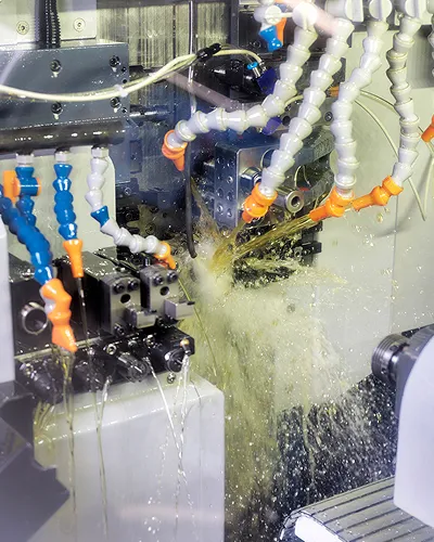CNC machine cutting metal while coolant sprays from flexible tubes with orange and blue tips.