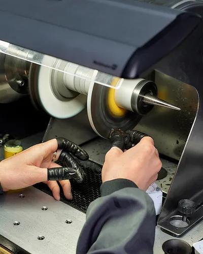 Hands wearing finger cots operating a polishing machine on a small metallic object.