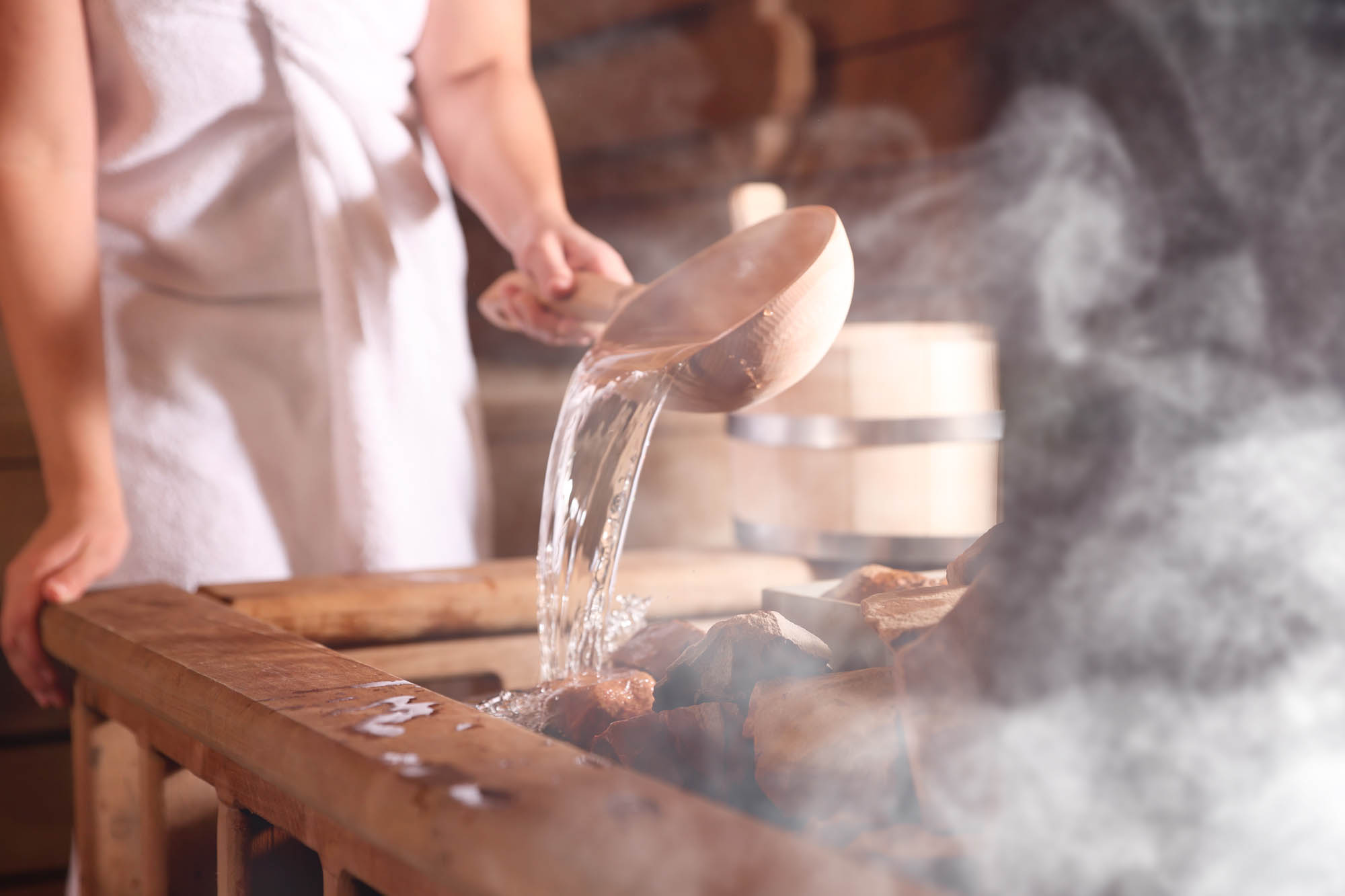 A Nordic sauna ritual — water poured over heated stones creating billowing steam in a traditional Scandinavian sauna