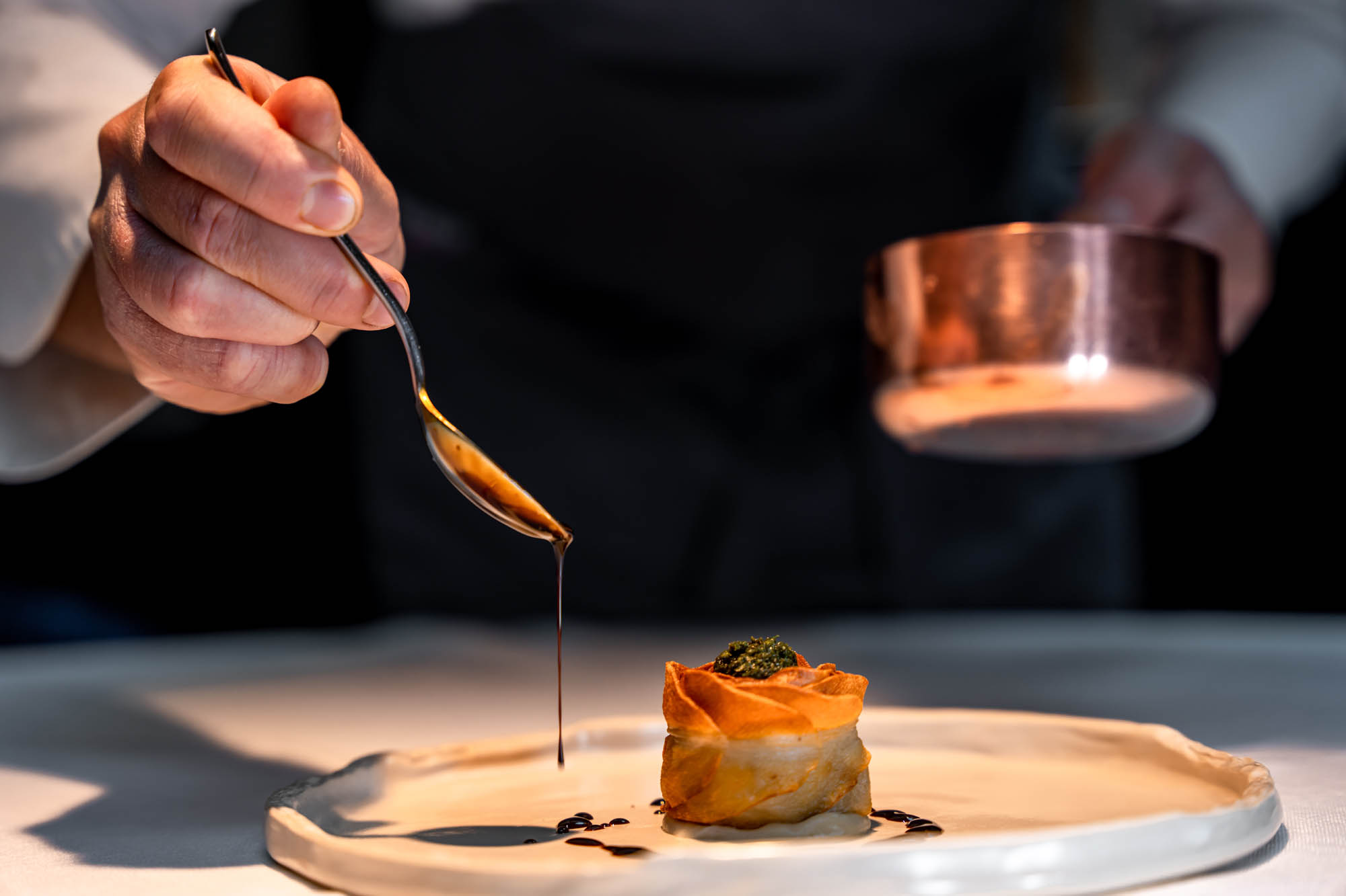 A chef drizzling sauce onto an elegantly plated dish at a Nordic fine-dining restaurant
