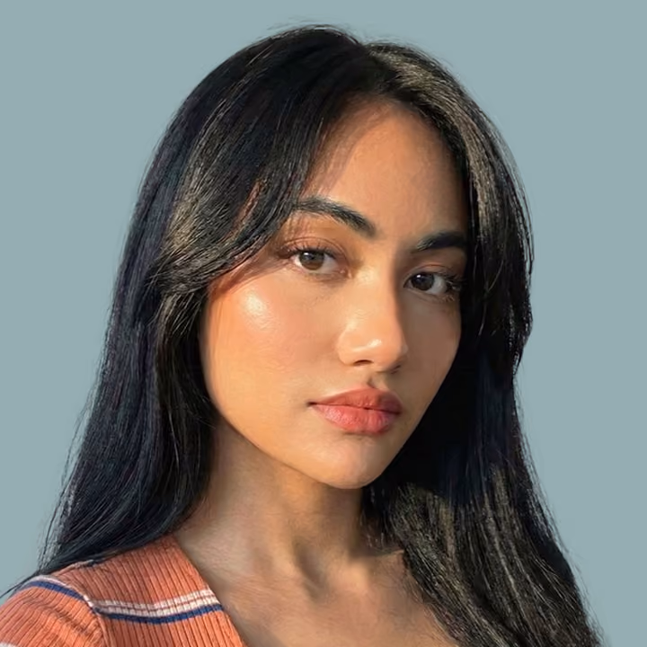 Young woman with long black hair and natural makeup wearing a striped top against a blue-gray background.