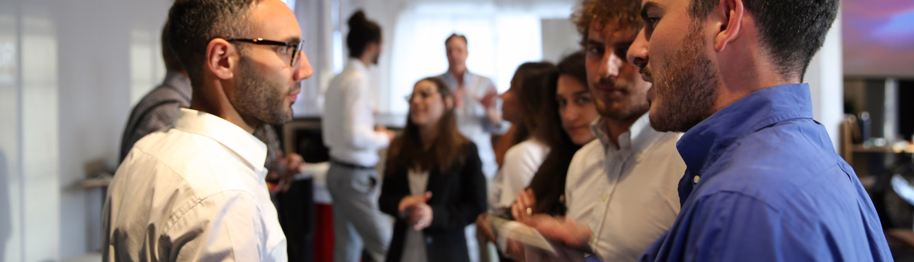 Group of professionals talking and networking in a bright office space during an event.