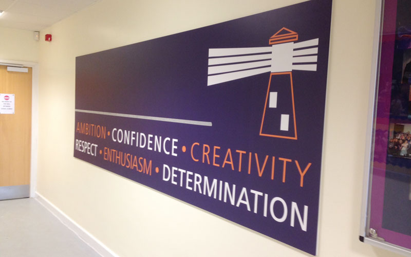 Sign on a wall with a lighthouse design and words: Ambition, Confidence, Creativity, Respect, Enthusiasm, Determination.