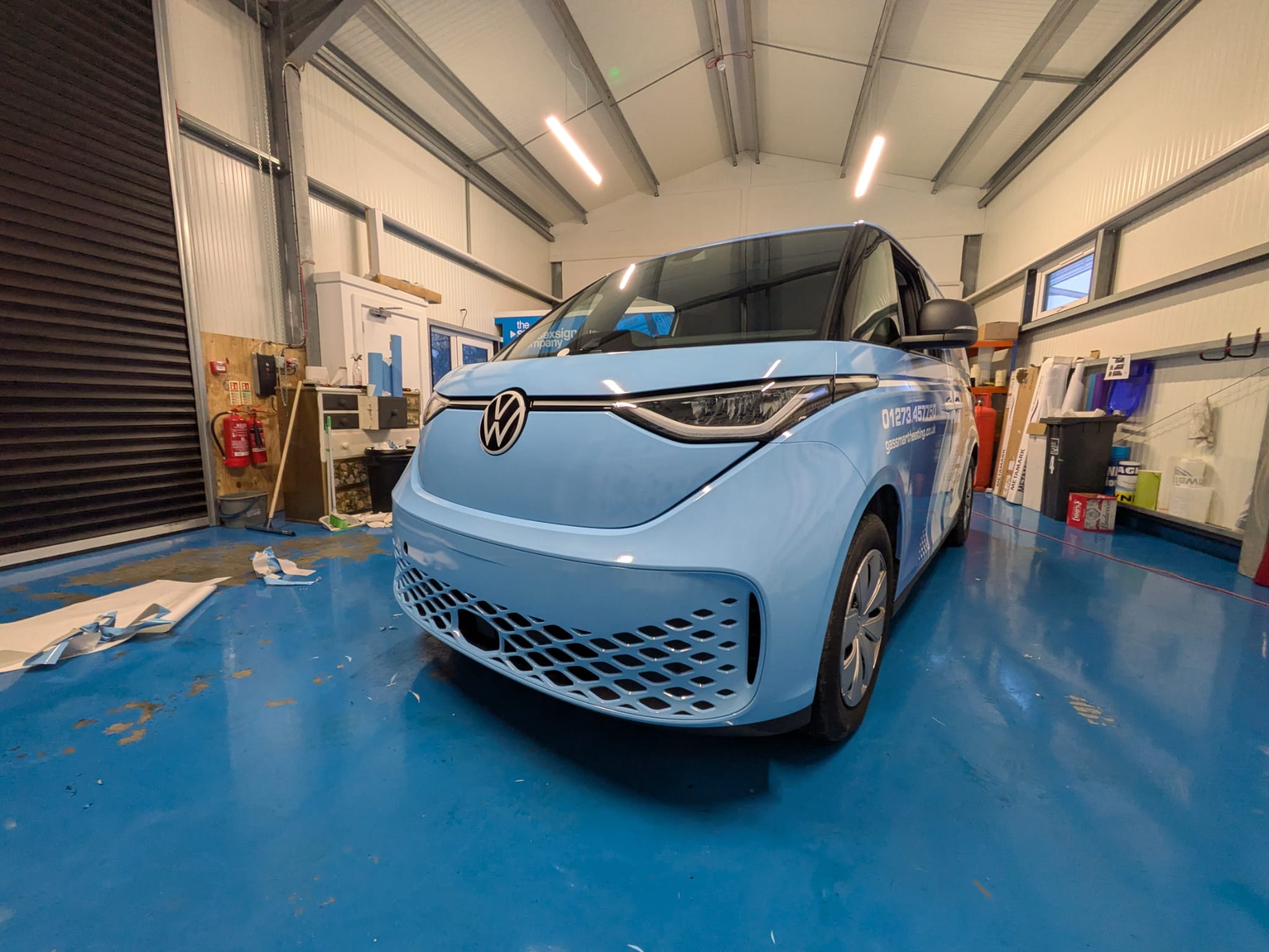 A light blue Volkswagen electric van parked in a garage with a shiny blue floor.