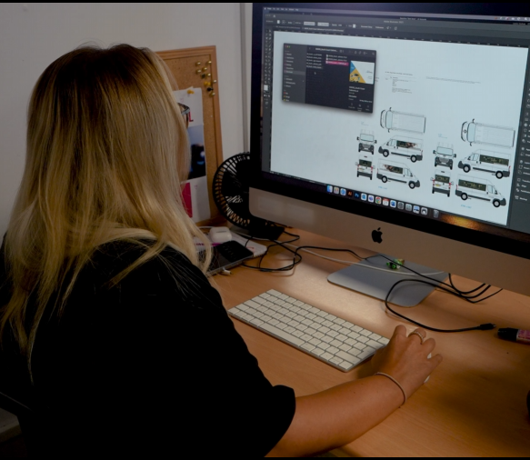 A person works on a large computer screen displaying vehicle design images.