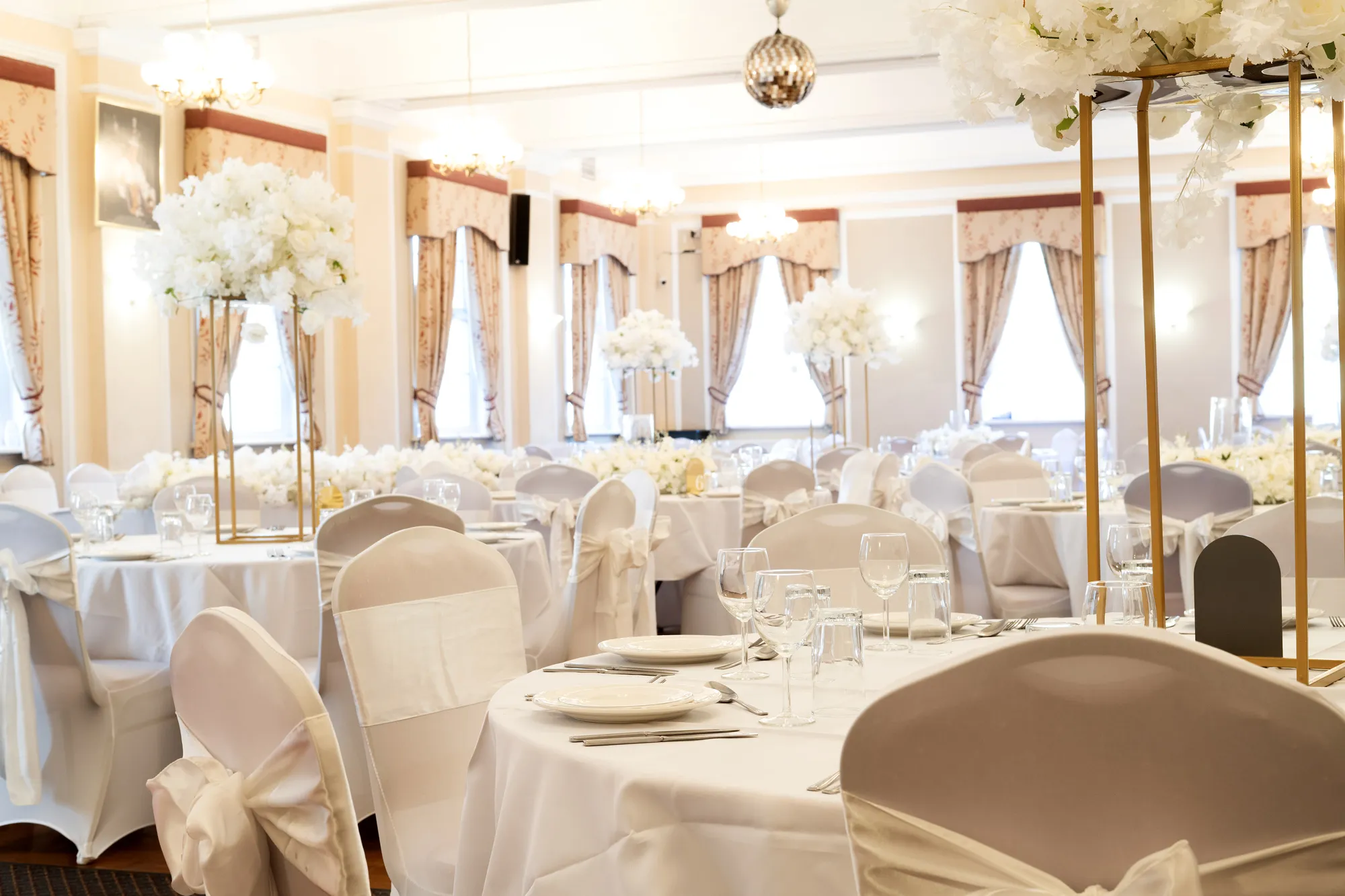 Elegant banquet hall with round tables, white chair covers, and tall floral centerpieces.