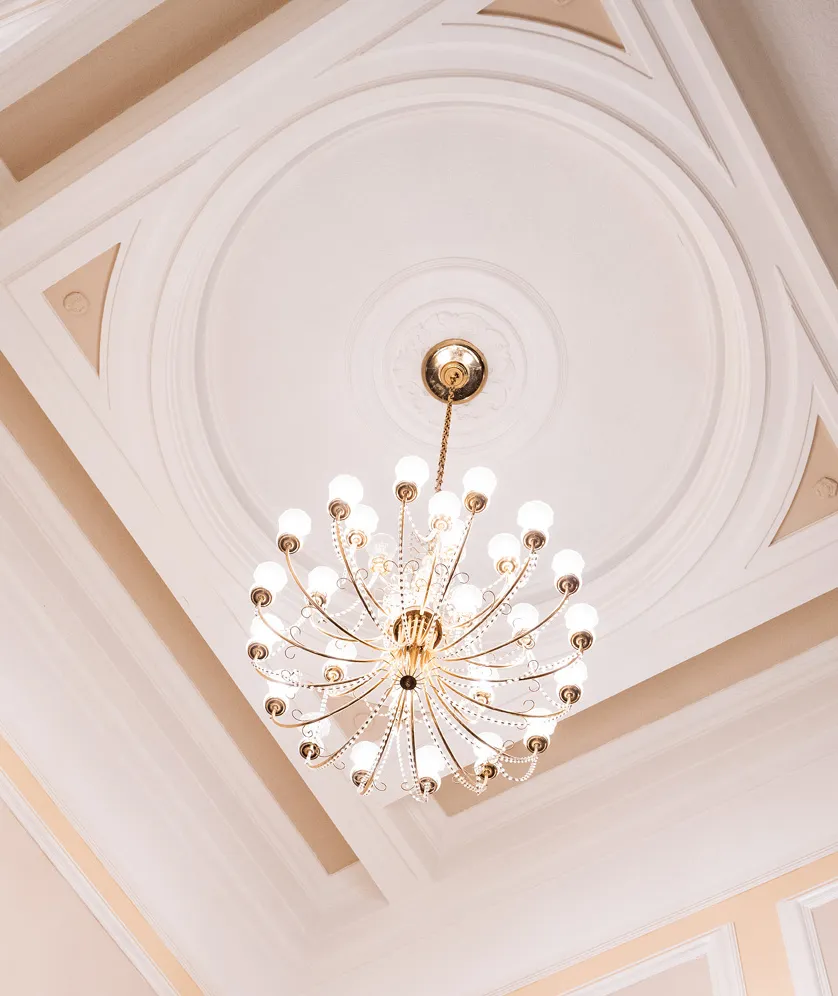 Large ornate chandelier with multiple glowing bulbs hanging from a decorative ceiling.