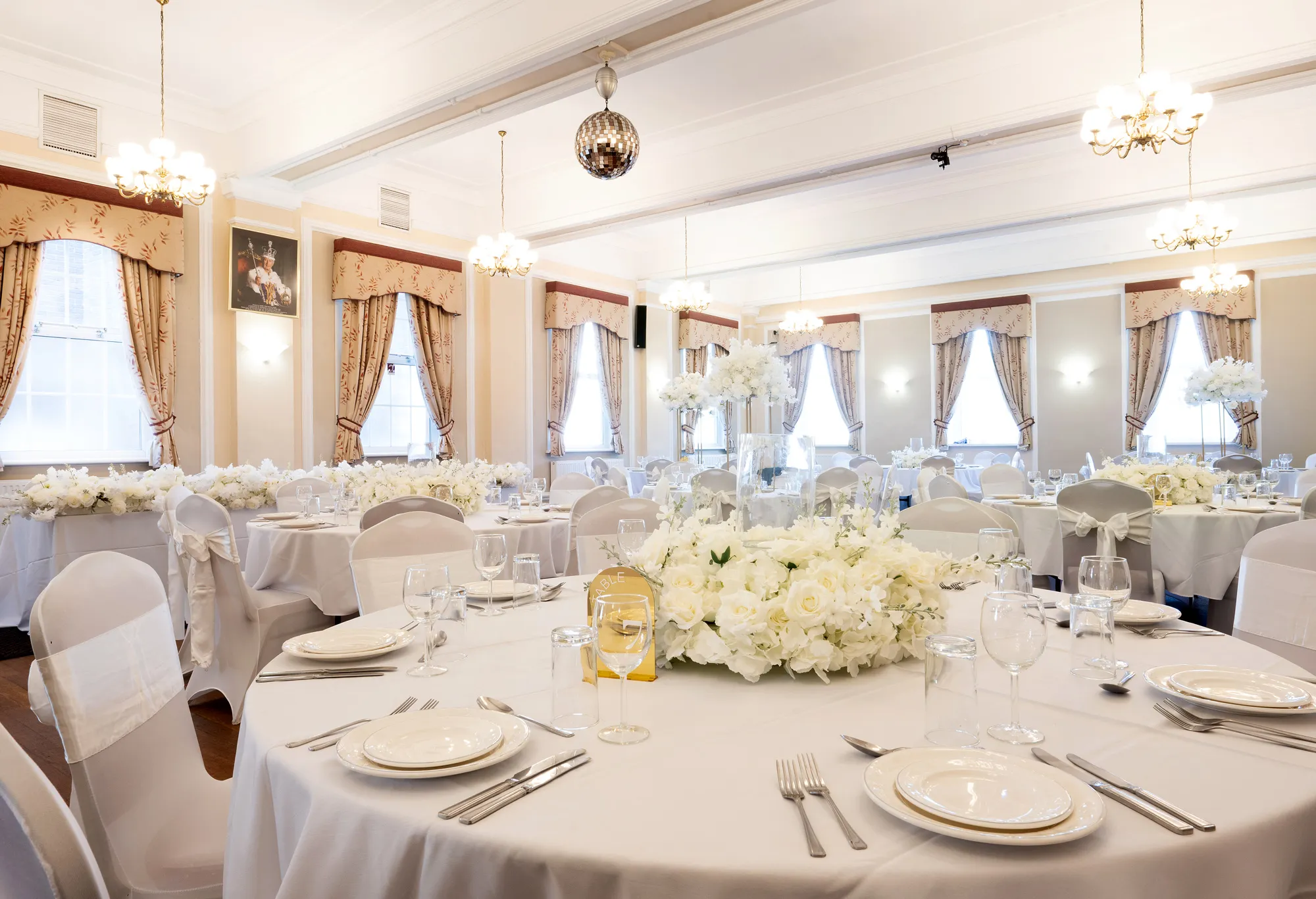 Elegant banquet hall with round tables set with white linens, plates, glassware, and floral centerpieces.