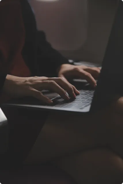 Person typing on a laptop keyboard in a dimly lit environment.