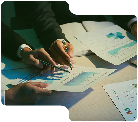 Two people reviewing and pointing at printed charts and graphs with pens on a table.