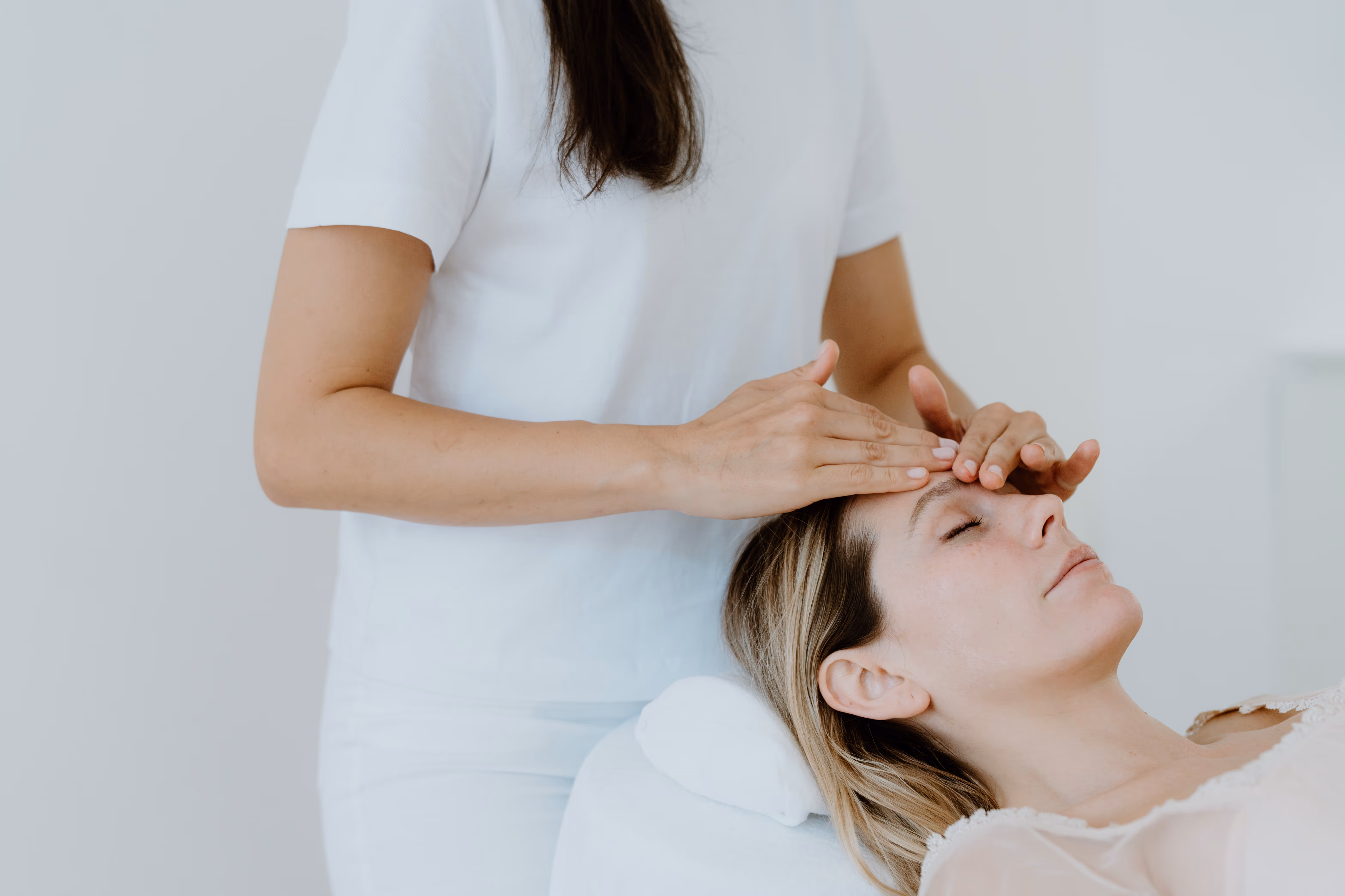 Frau erhält eine entspannende Gesichtsbehandlung, während sie mit geschlossenen Augen auf einer Liege liegt.