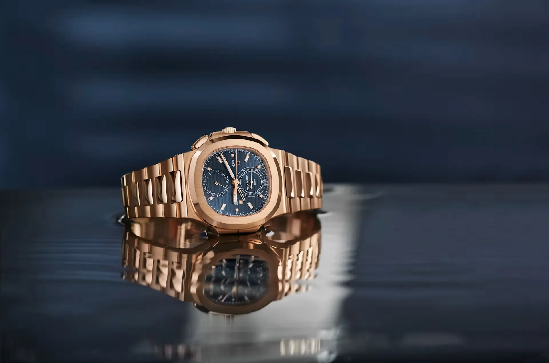 Rose gold wristwatch with a dark blue dial reflecting on a glossy surface.