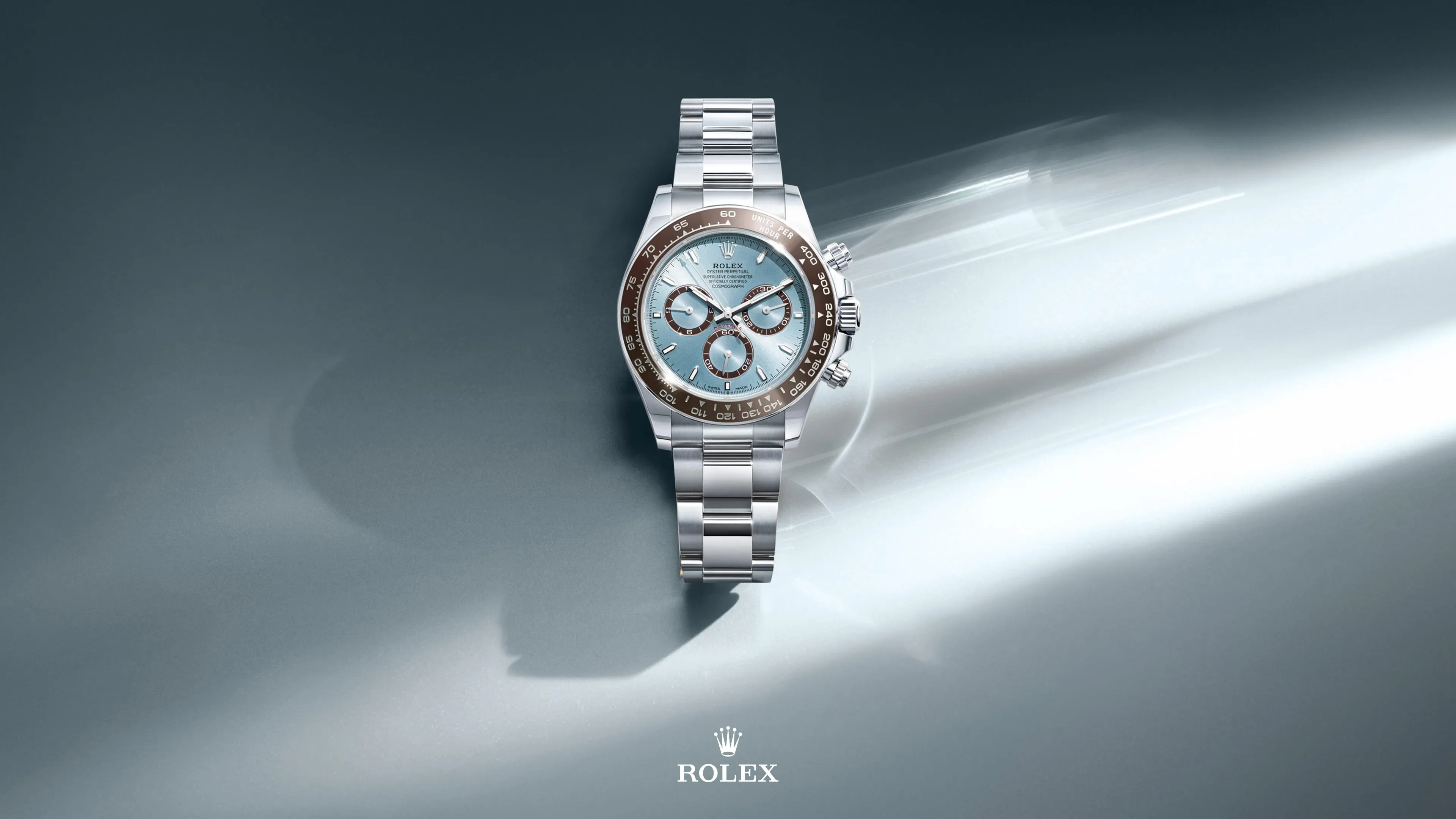 Rolex stainless steel wristwatch with a light blue dial and three subdials on a gradient gray background with a light beam.