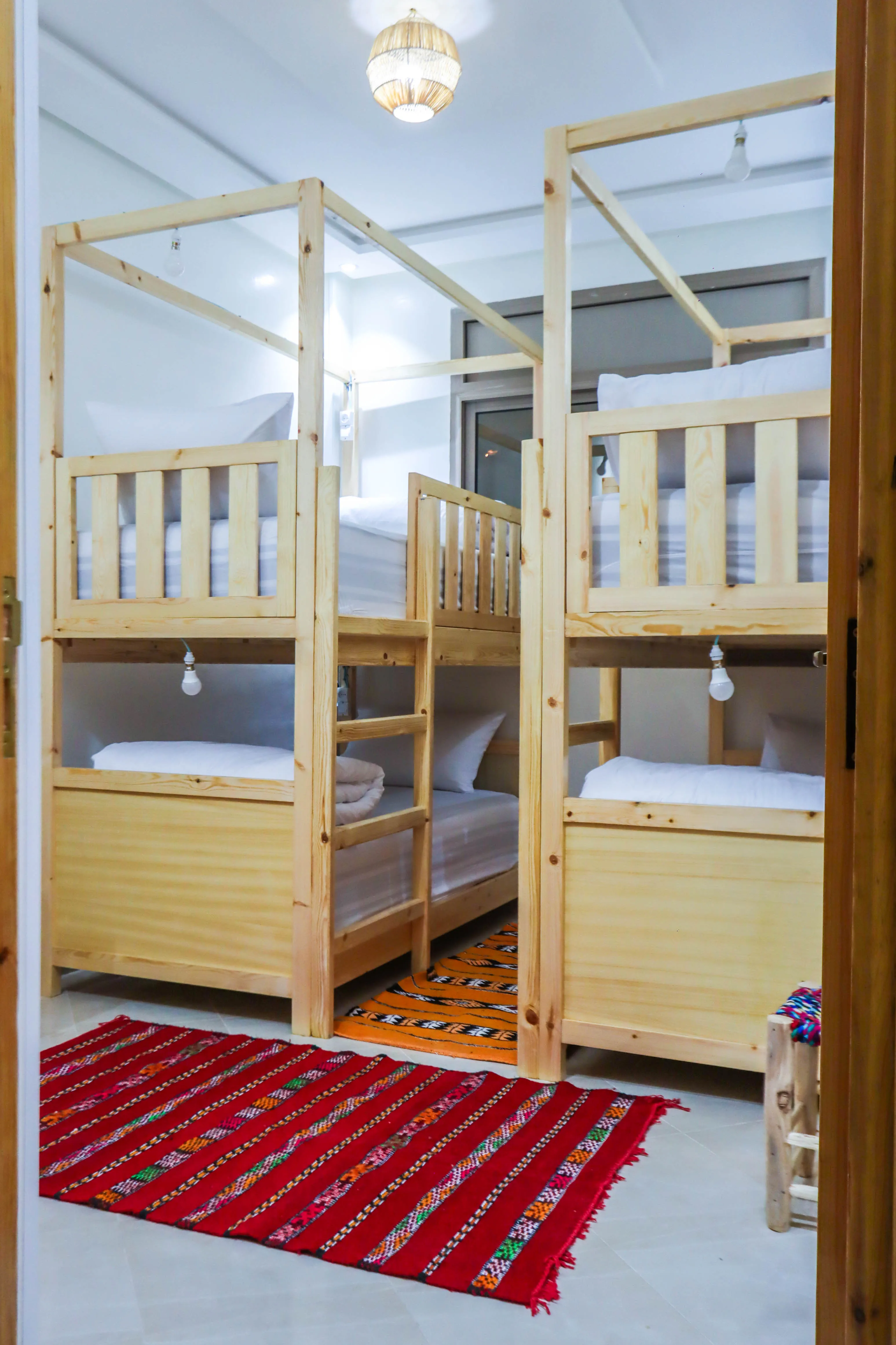 Room with two wooden bunk beds featuring white bedding and colorful rugs on the floor.