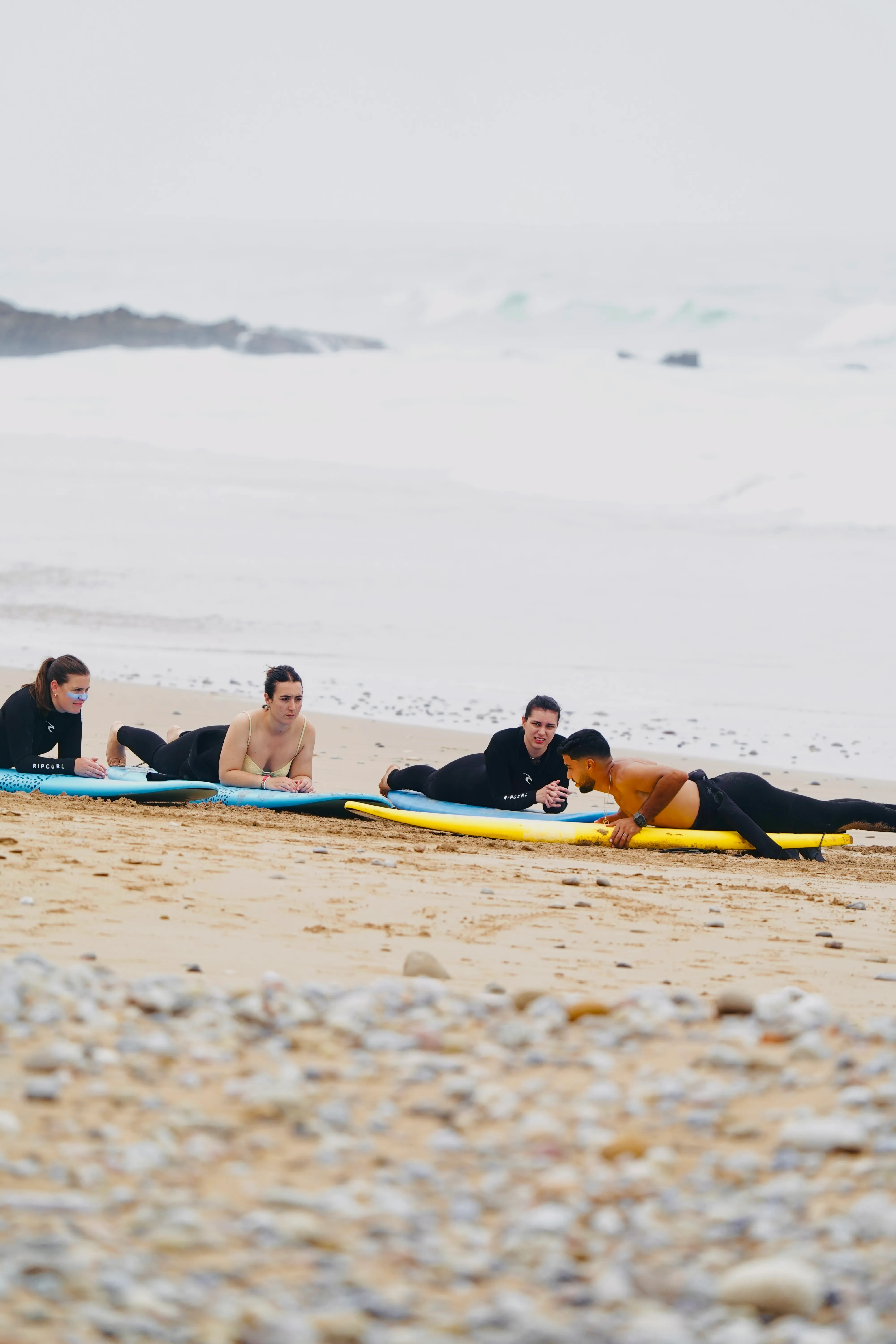 Surfing instructor teaching three students lying on surfboards on a sandy beach.