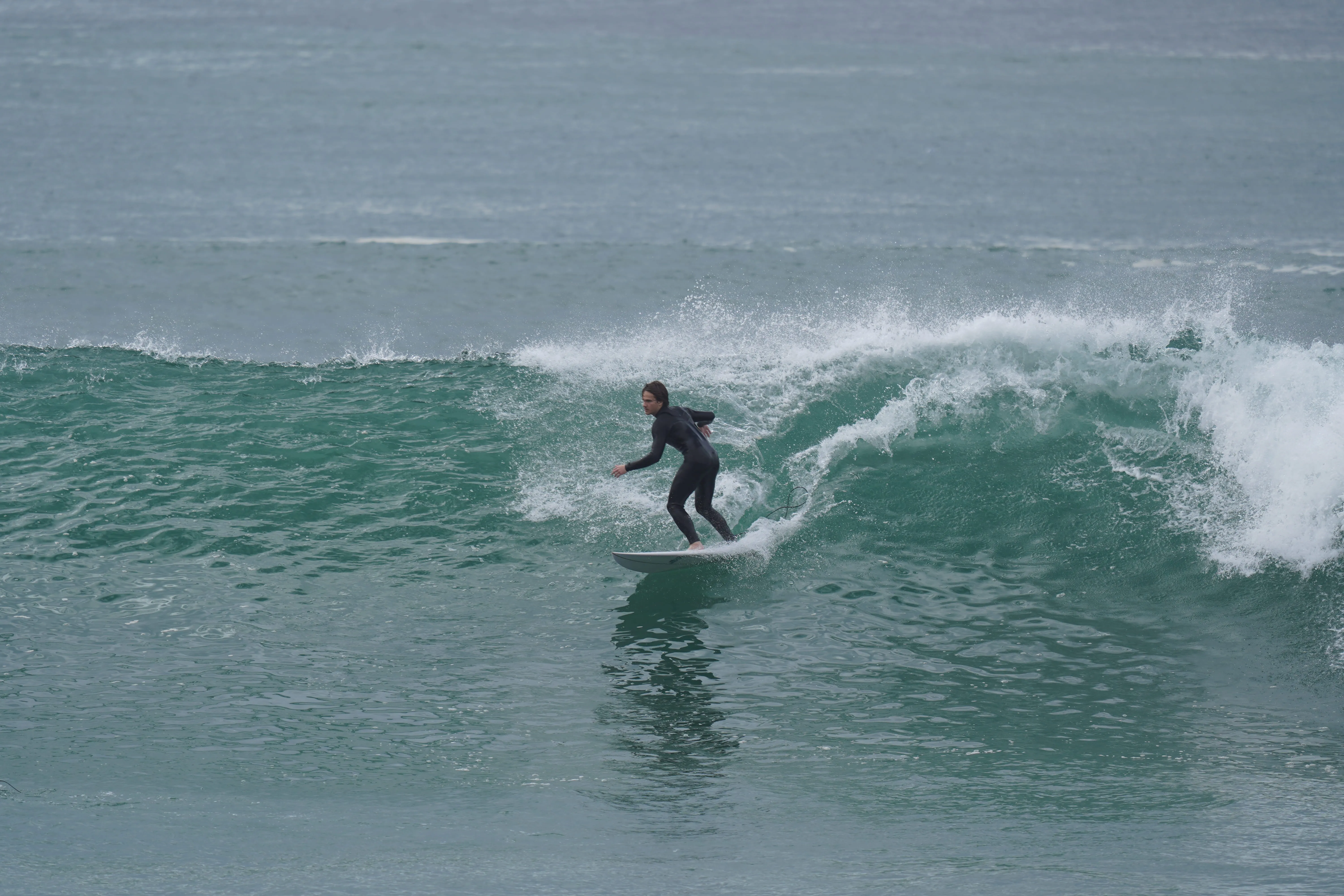 Surfer in a black wetsuit riding a turquoise ocean wave with white spray.